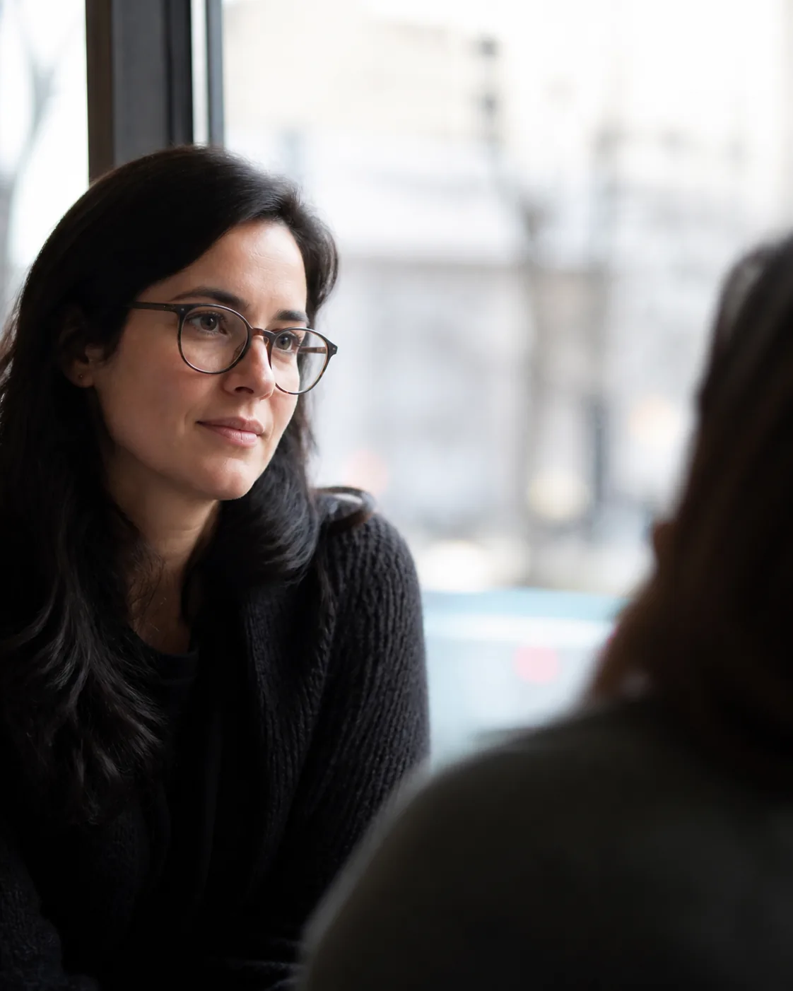 A person wearing ordinary eyeglasses listening attentively in a café conversation